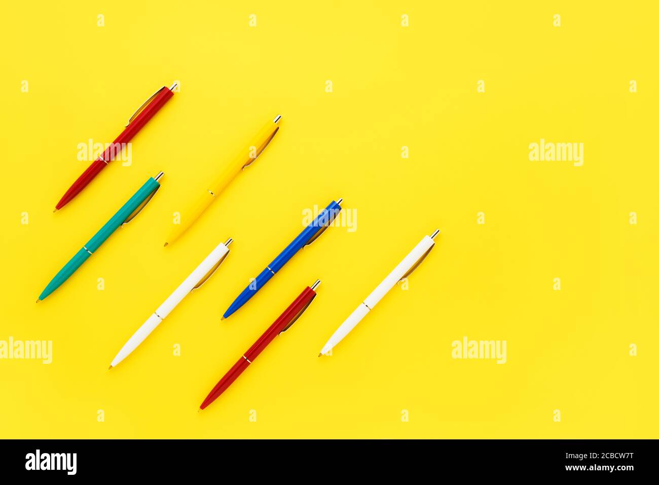 Seven colorful ballpoint pens on a bright yellow background. Top view