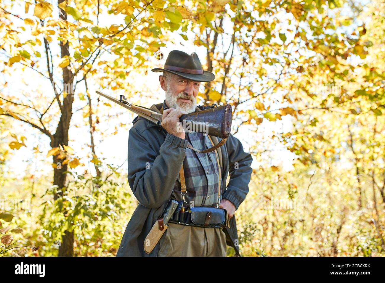Satisfied hunter carry rifle gun on shoulder, looking at camera.Autumn