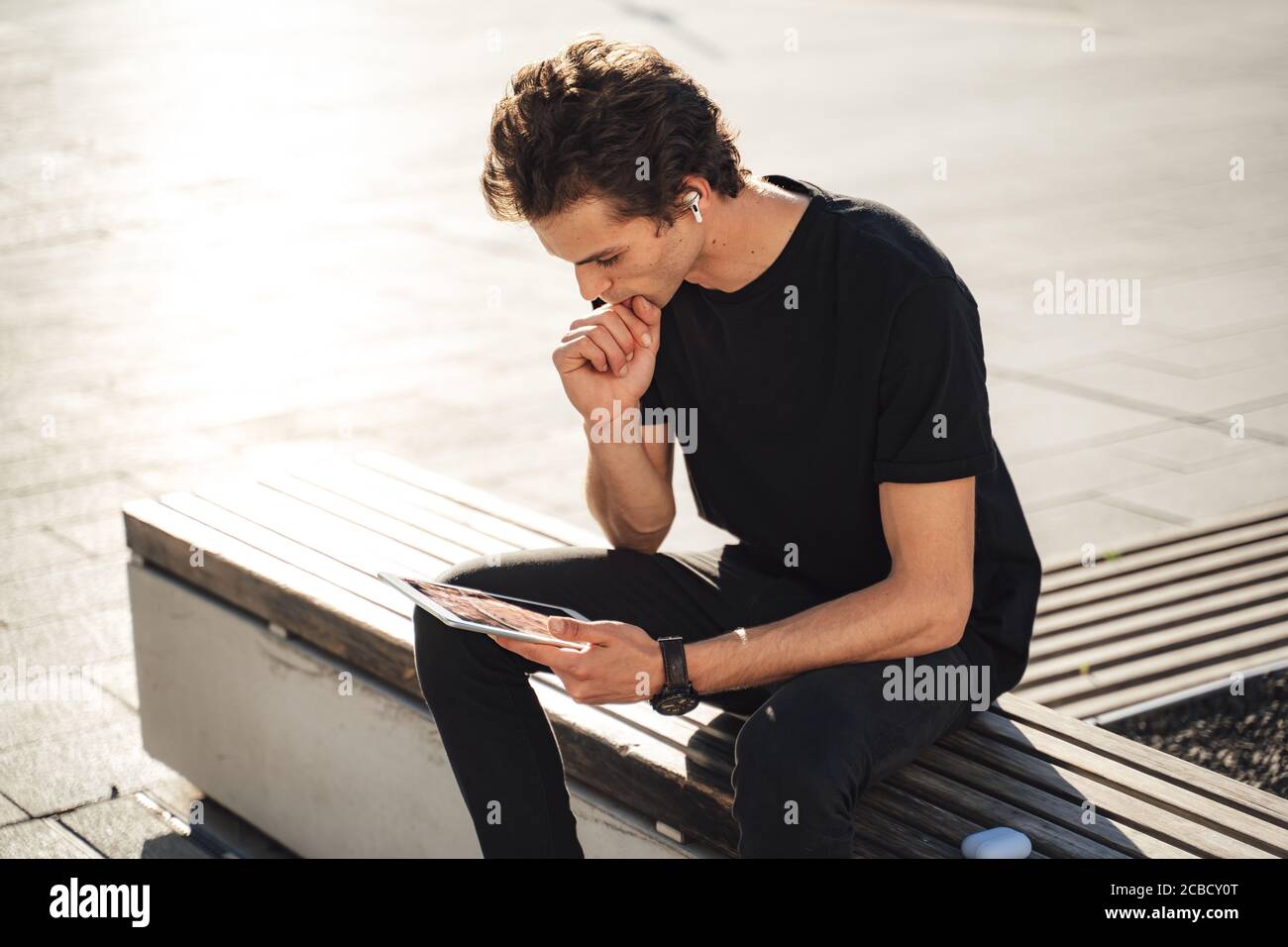 Young university student studying online on tablet computer while sitting on bench at campus Stock Photo