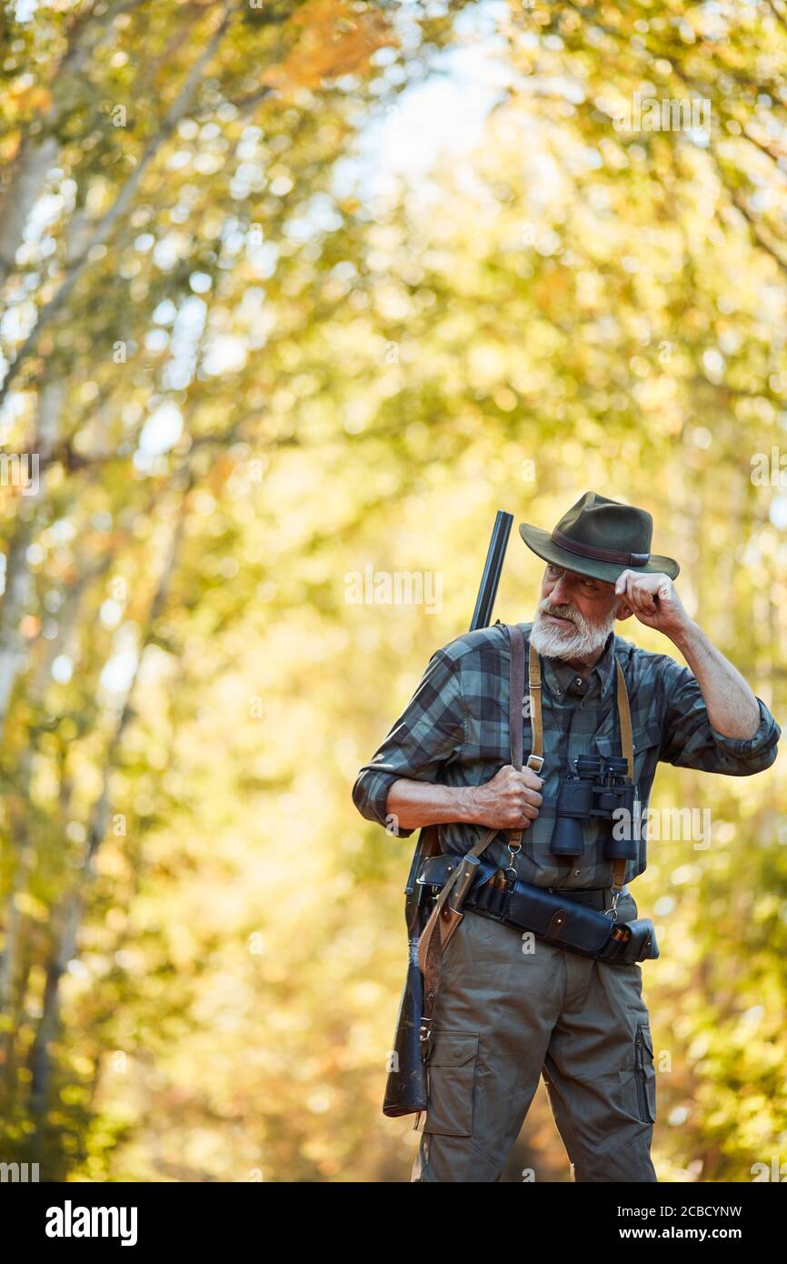 Caucasian older hunter stand in autumn forest, look away, straighten