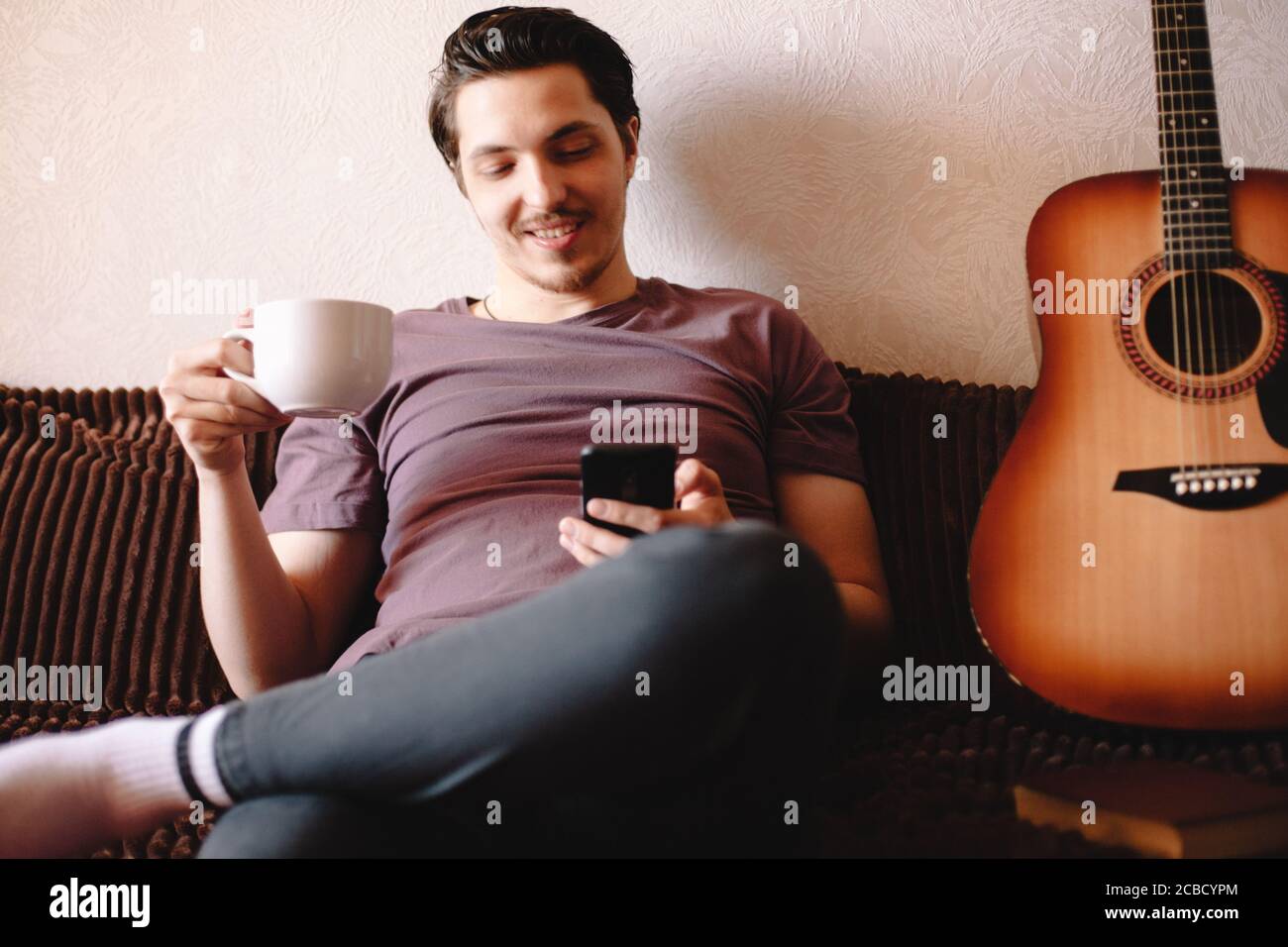 Happy young man using smart phone while drinking tea at home Stock Photo
