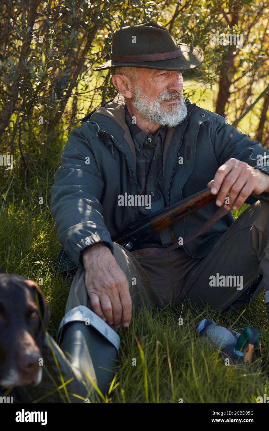 Senior hunter with gun sit on grass with dog after hunting Stock Photo