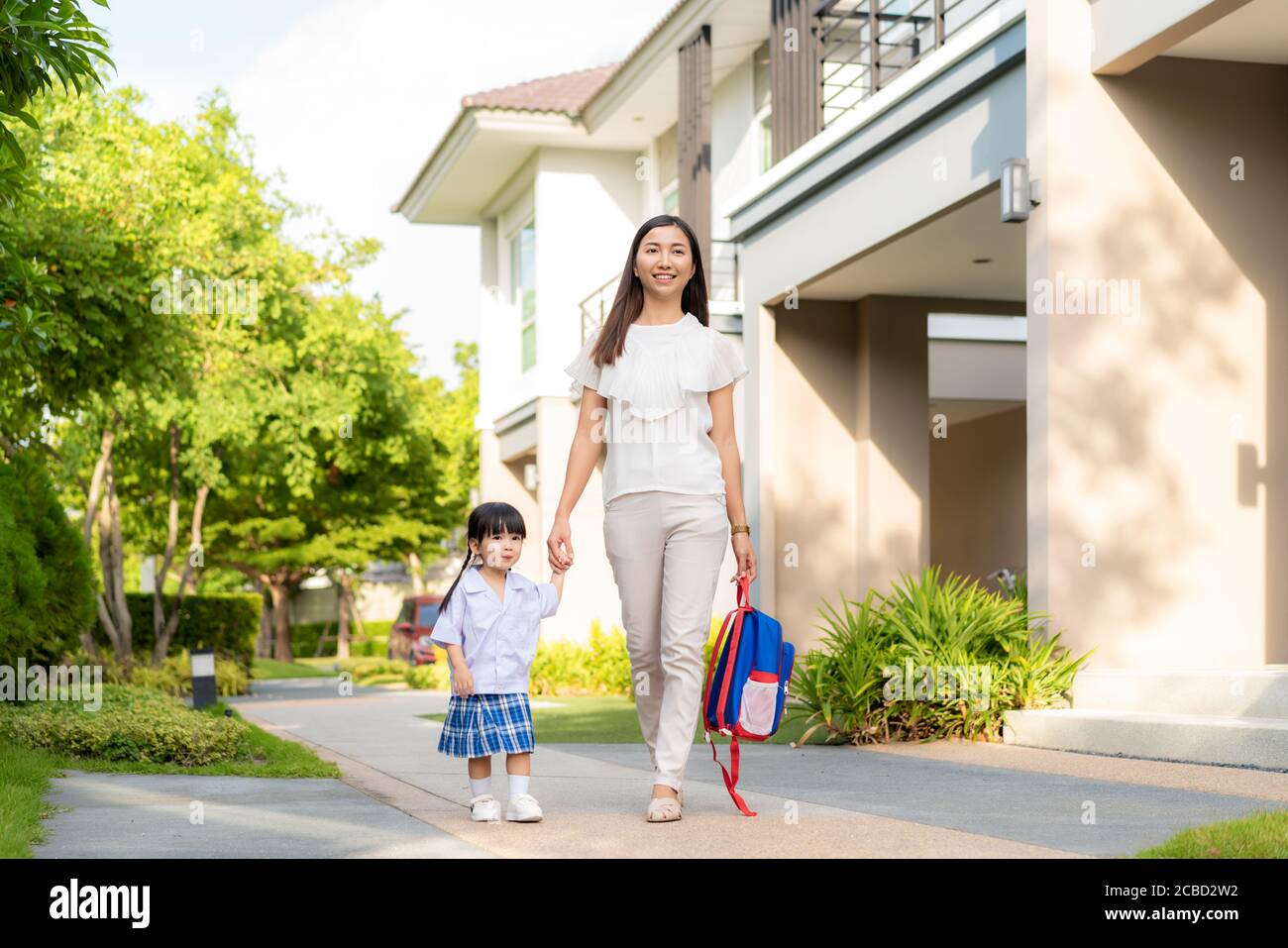 Happy Asian mother and daughter kindergarten student walking to school at morning school routine. Beginning of lessons. First day of fall. Parenthood Stock Photo