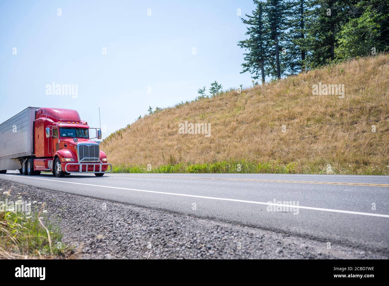 Loaded industrial red big rig semi truck with grille guard transporting frozen commercial cargo in long refrigerator semi trailer running on the windi Stock Photo