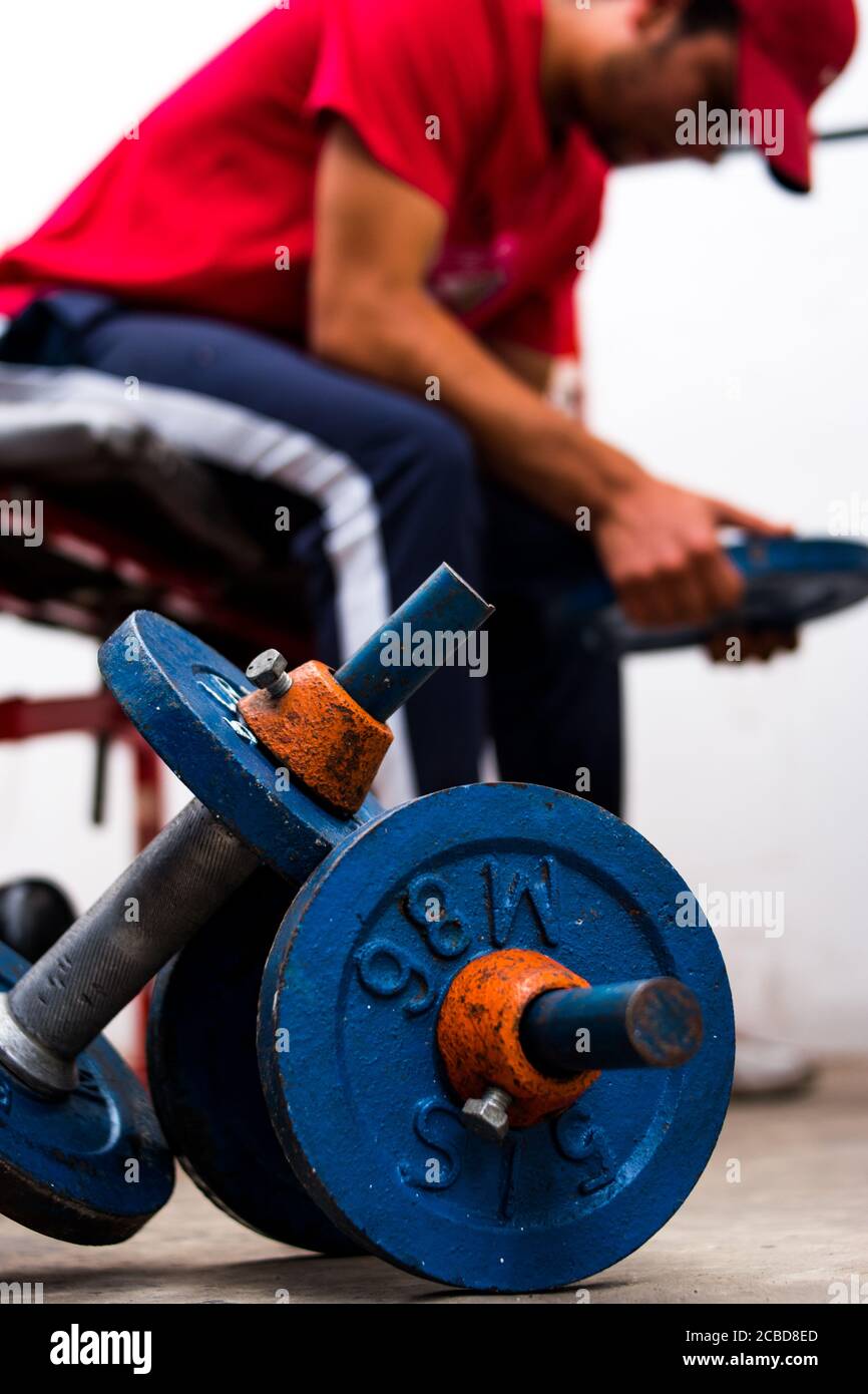 Young man lifting old blue gym weights on the floor in a gym Stock