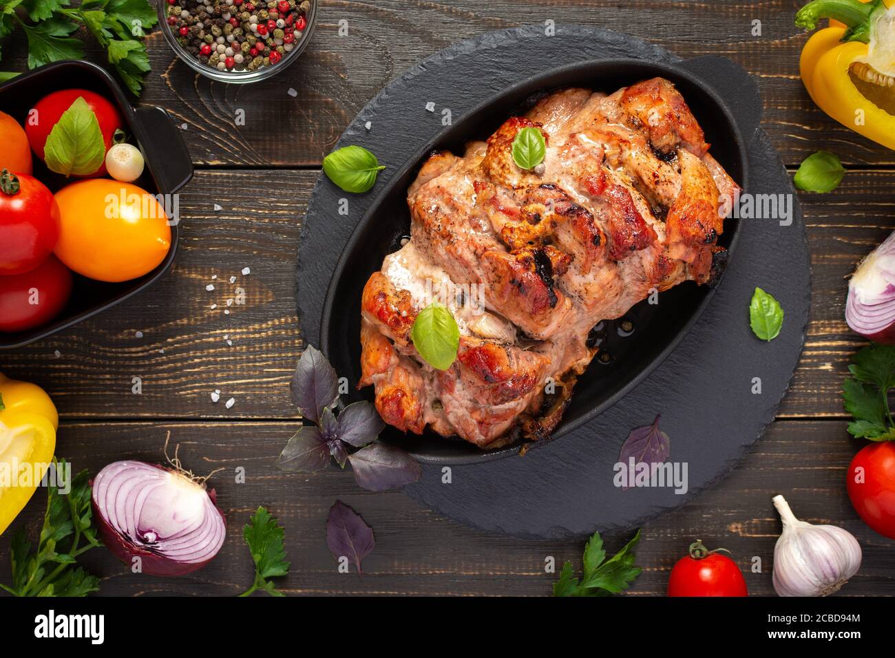 Baked pork ham on a wooden background, fried piece of meat with spices, fresh vegetables, top view Stock Photo