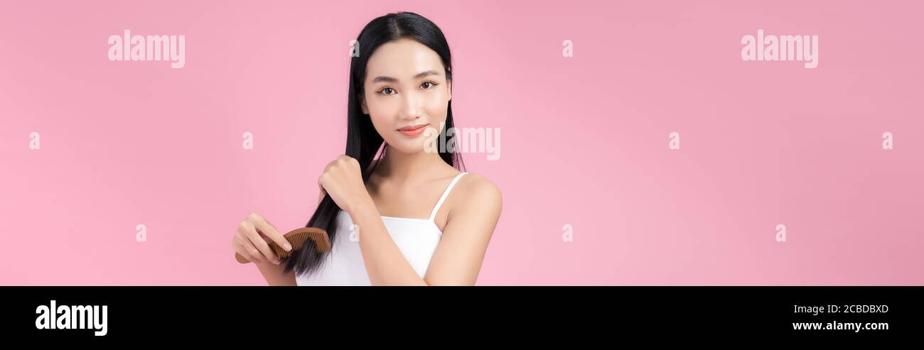 Portrait of beautiful young Asian woman combing her hair, looking at camera and smiling Stock Photo