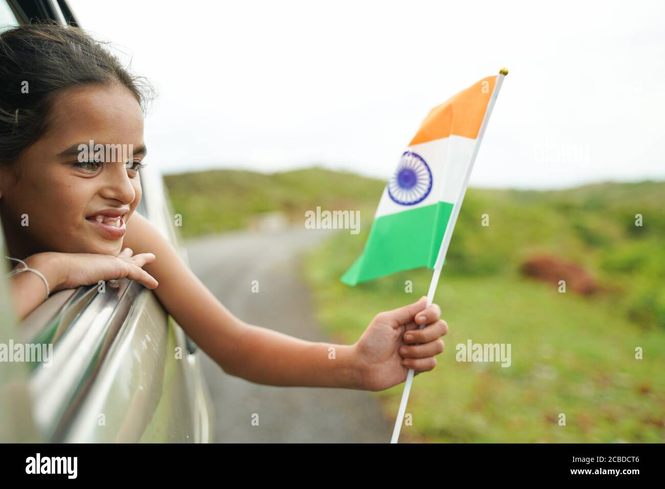 Happy Cheerful Young girl kid holding Indian flag out of in moving car window - Concept of patriotism and Independence or republic day celebration Stock Photo