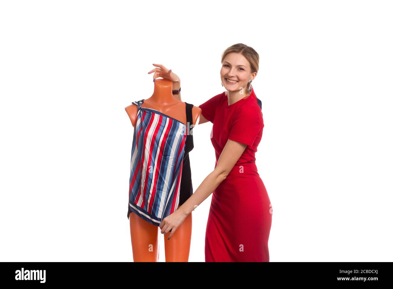 A young woman in a red dress puts a striped dress on a mannequin. isolated on white Stock Photo