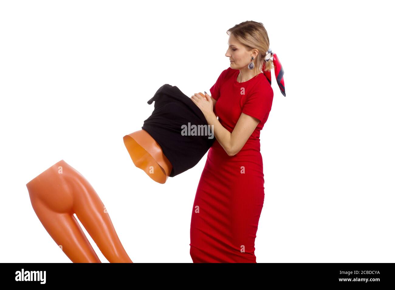 A young woman in a red dress, puts a black dress on a mannequin. The