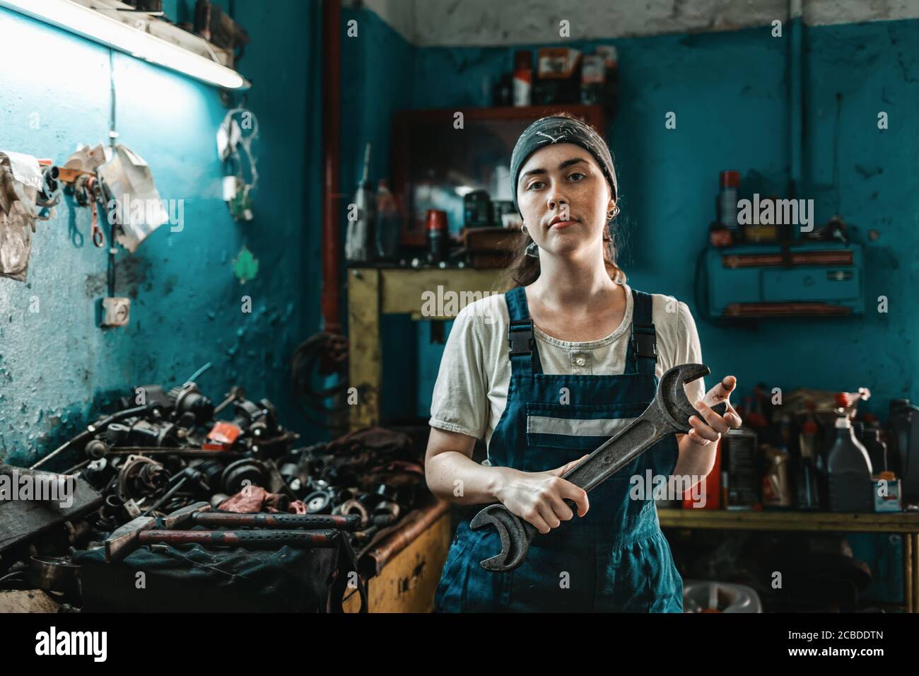 The concept of small business, feminism and women's equality. A young woman in overalls poses with a large wrench in her hands. Stock Photo