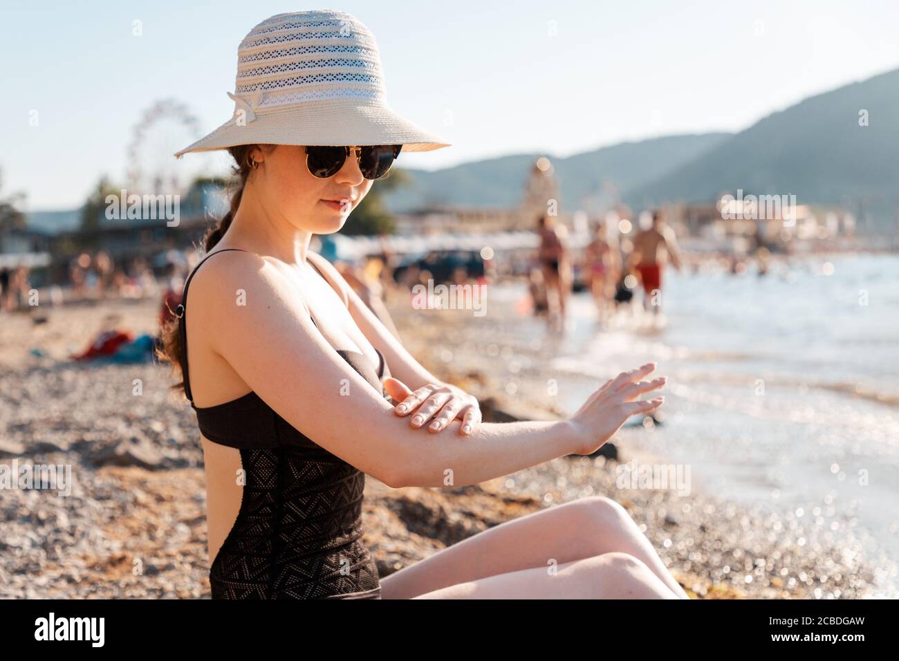 https://c8.alamy.com/comp/2CBDGAW/a-woman-in-a-straw-hat-and-glasses-smears-sunscreen-sitting-on-the-beach-the-concept-of-proper-tanning-2CBDGAW.jpg
