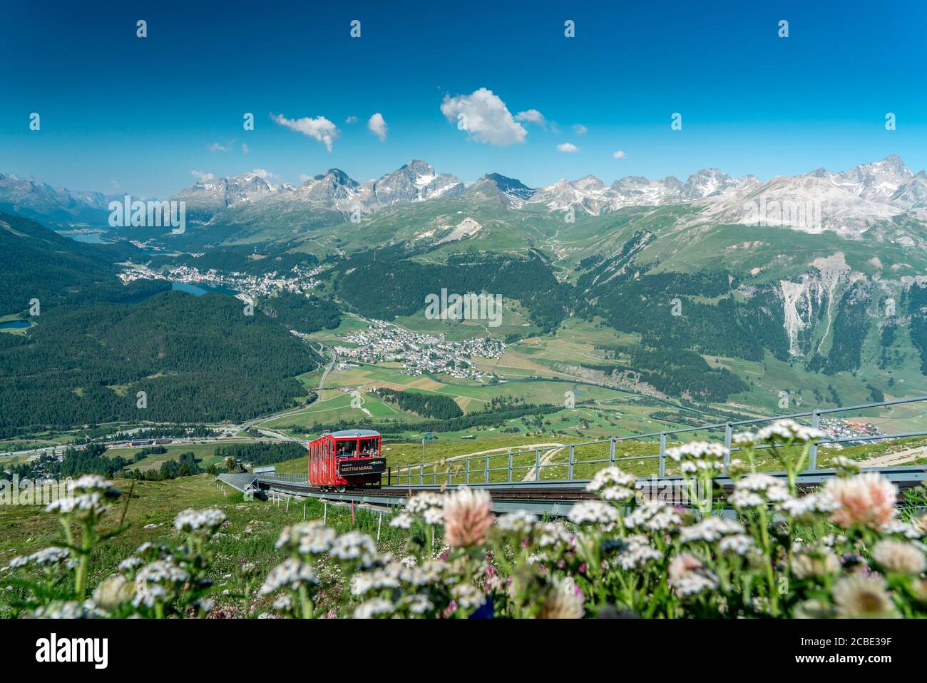 Red funicular uphill crossing the green meadows in summer, Muottas Muragl, canton of Graubunden, Engadine, Switzerland Stock Photo