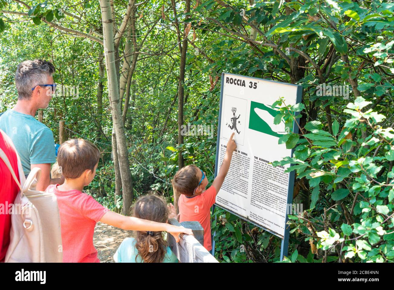 Father with children looks at the information sign at Naquane National Park of Rupestrian Engravings, Valcamonica, Lombardy, Italy Stock Photo