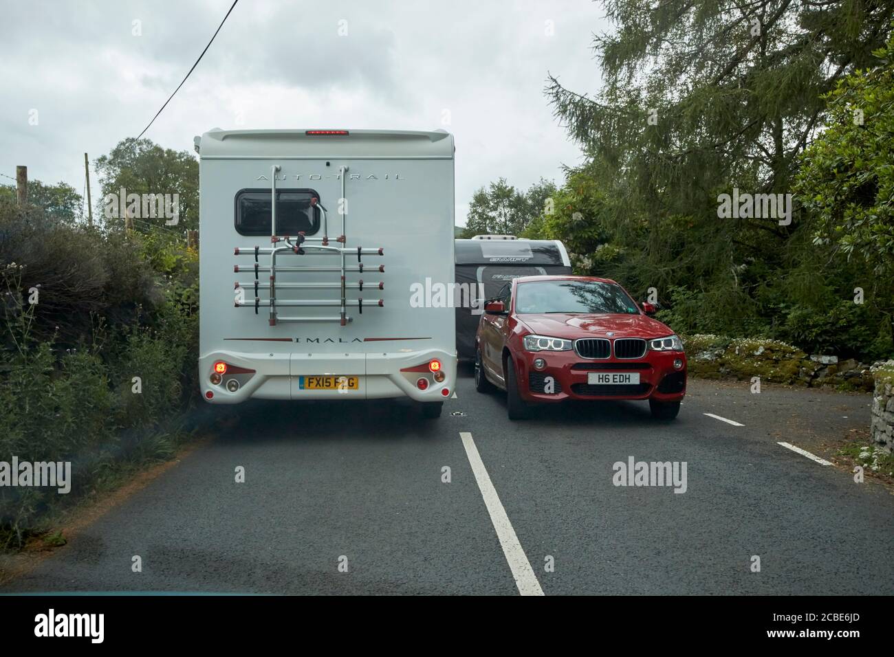 looking through windscreen at road block caused by car towing caravan meeting motorhome on narrow road near coniston in the lake district cumbria engl Stock Photo