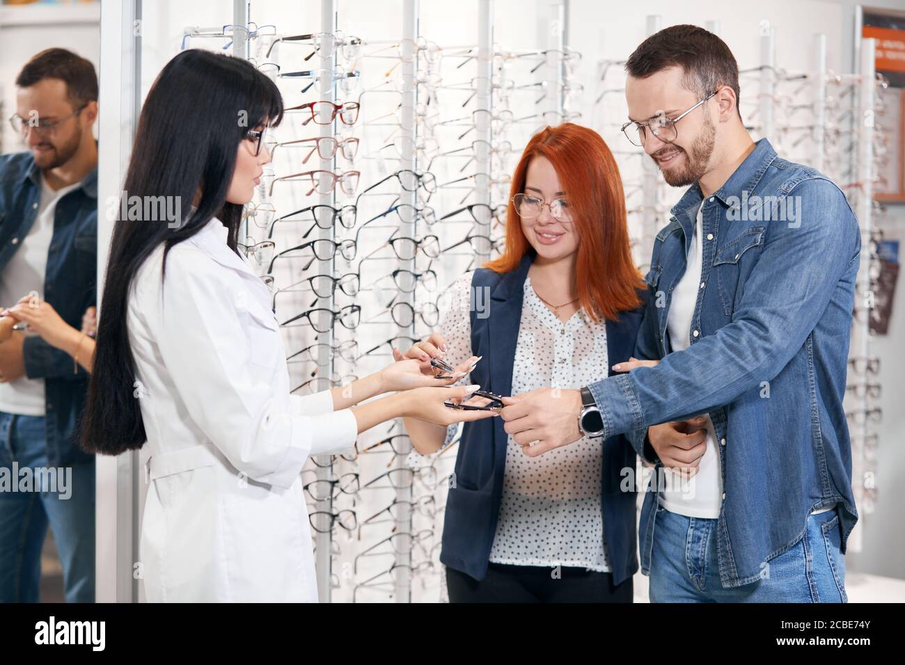 Asian ophthalmologist and young couple choosing glasses in modern 