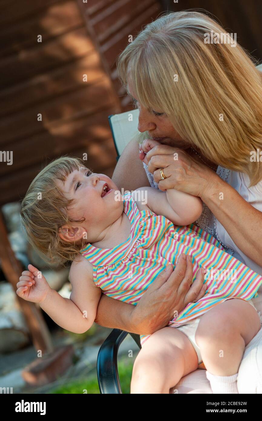 Happy child laughing and looking up lovingly at grandparent while sitting on lap outdoors Stock Photo