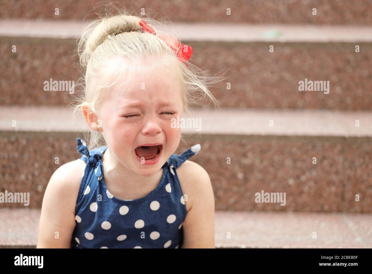 little girl in a blue dress sits on the steps and cries Stock Photo - Alamy