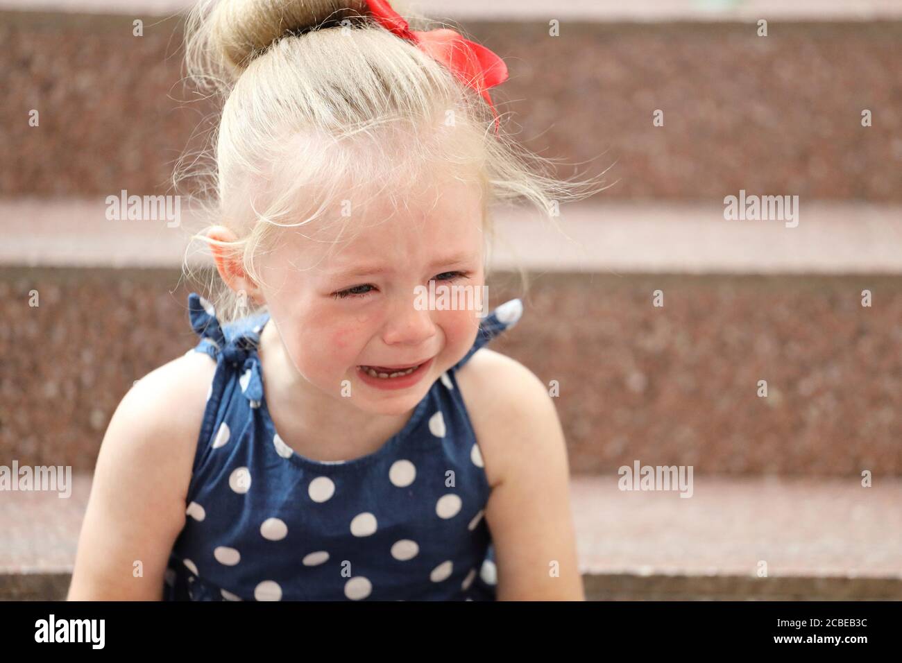 little girl in a blue dress sits on the steps and cries Stock Photo - Alamy