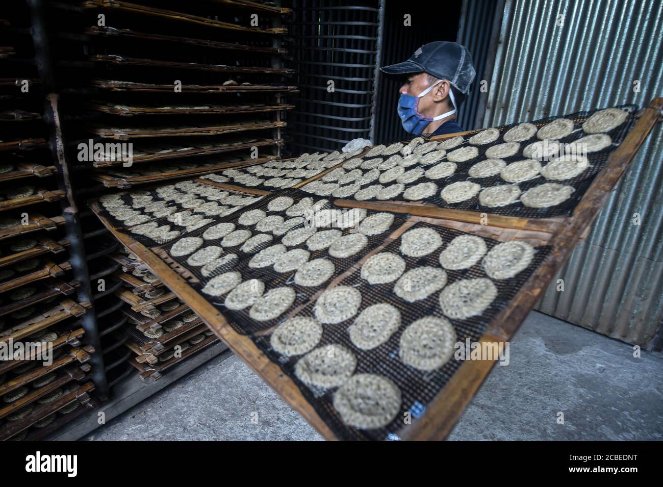 (200813) -- WEST JAVA, Aug. 13, 2020 (Xinhua) -- A worker wearing a face mask holds steamed crackers to be dried in an oven at a cracker factory in Depok, West Java, Indonesia, Aug. 13, 2020. Indonesia will distribute working capital assistance for 9 million small and medium enterprises (SMEs) to help them revive businesses which have been dashed by the novel coronavirus pandemic, a minister said here on Wednesday. ( Xinhua/Agung Kuncahya B.) Stock Photo