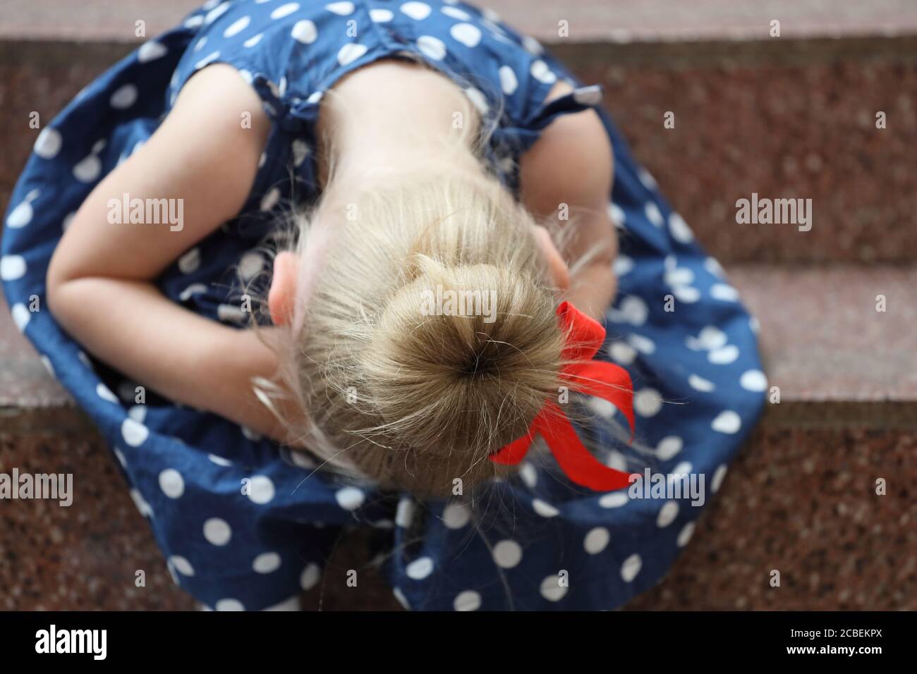 little girl in a blue dress sits on the steps and cries Stock Photo - Alamy