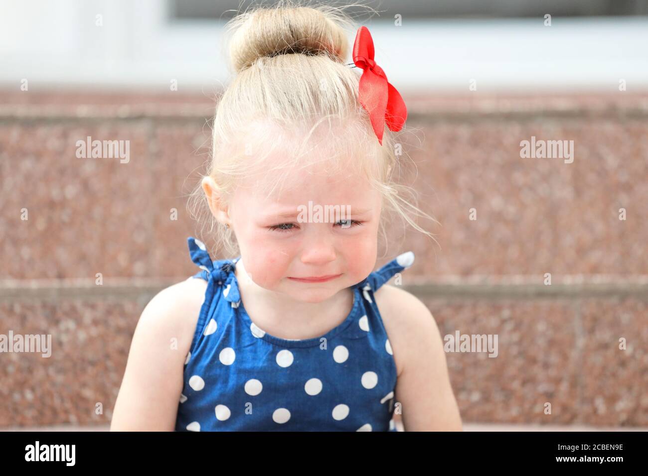 little girl in a blue dress sits on the steps and cries Stock Photo - Alamy