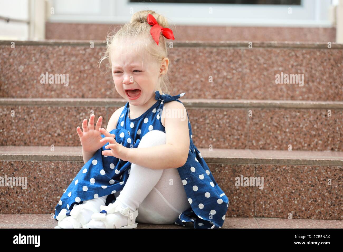 little girl in a blue dress sits on the steps and cries Stock Photo - Alamy