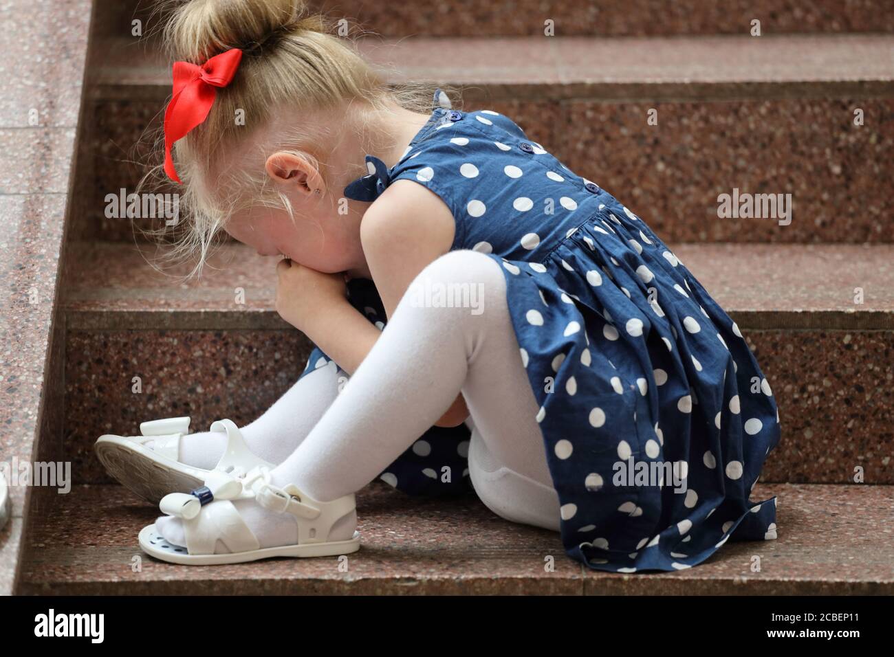 little girl in a blue dress sits on the steps and cries Stock Photo - Alamy