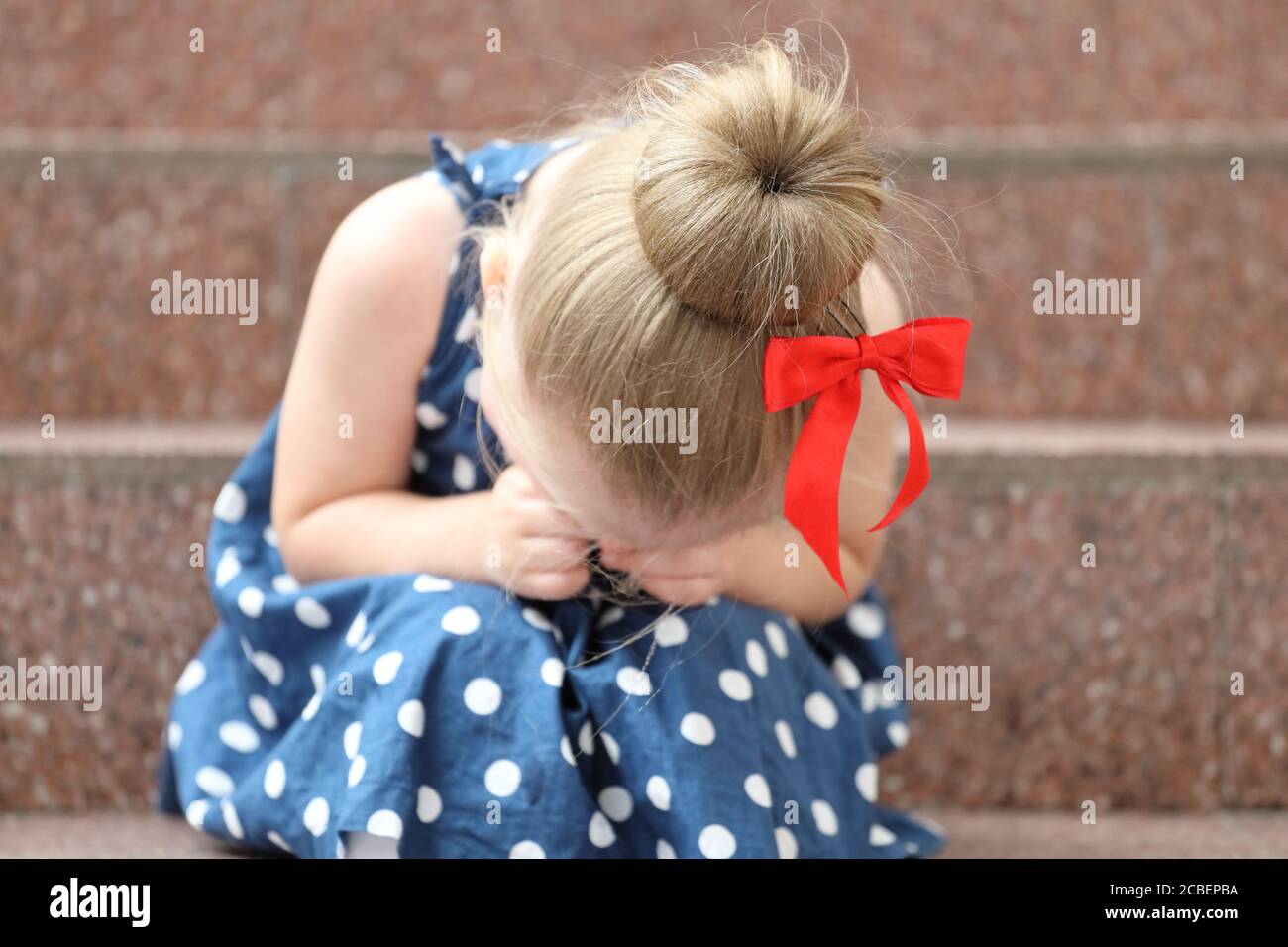 little girl in a blue dress sits on the steps and cries Stock Photo - Alamy