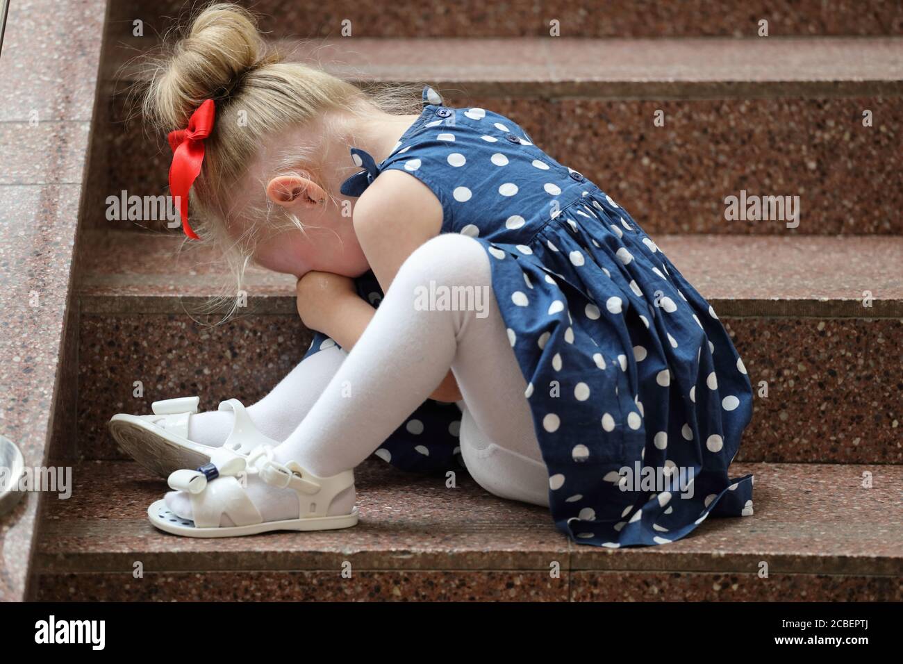little girl in a blue dress sits on the steps and cries Stock Photo - Alamy