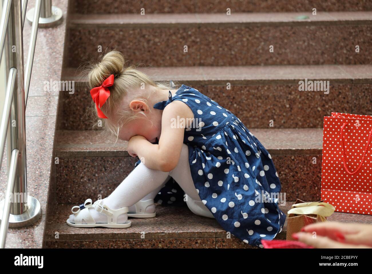 little girl in a blue dress sits on the steps and cries Stock Photo - Alamy