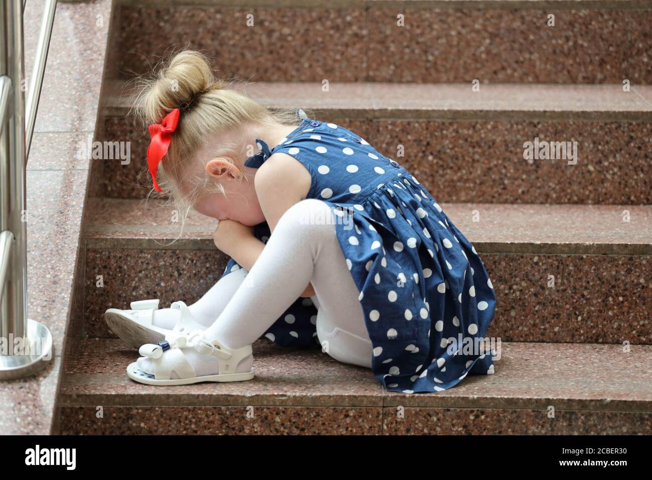 little girl in a blue dress sits on the steps and cries Stock Photo - Alamy