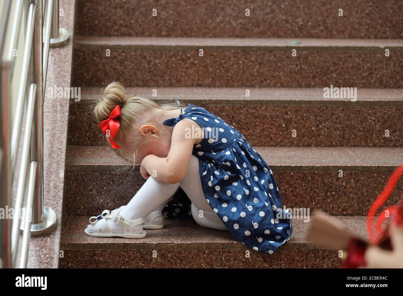 little girl in a blue dress sits on the steps and cries Stock Photo - Alamy