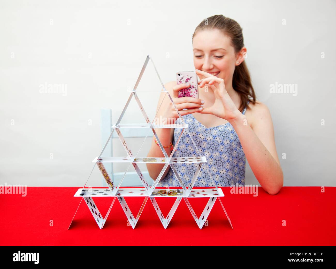 A teenage girl photographing a house of cards she has built Stock Photo