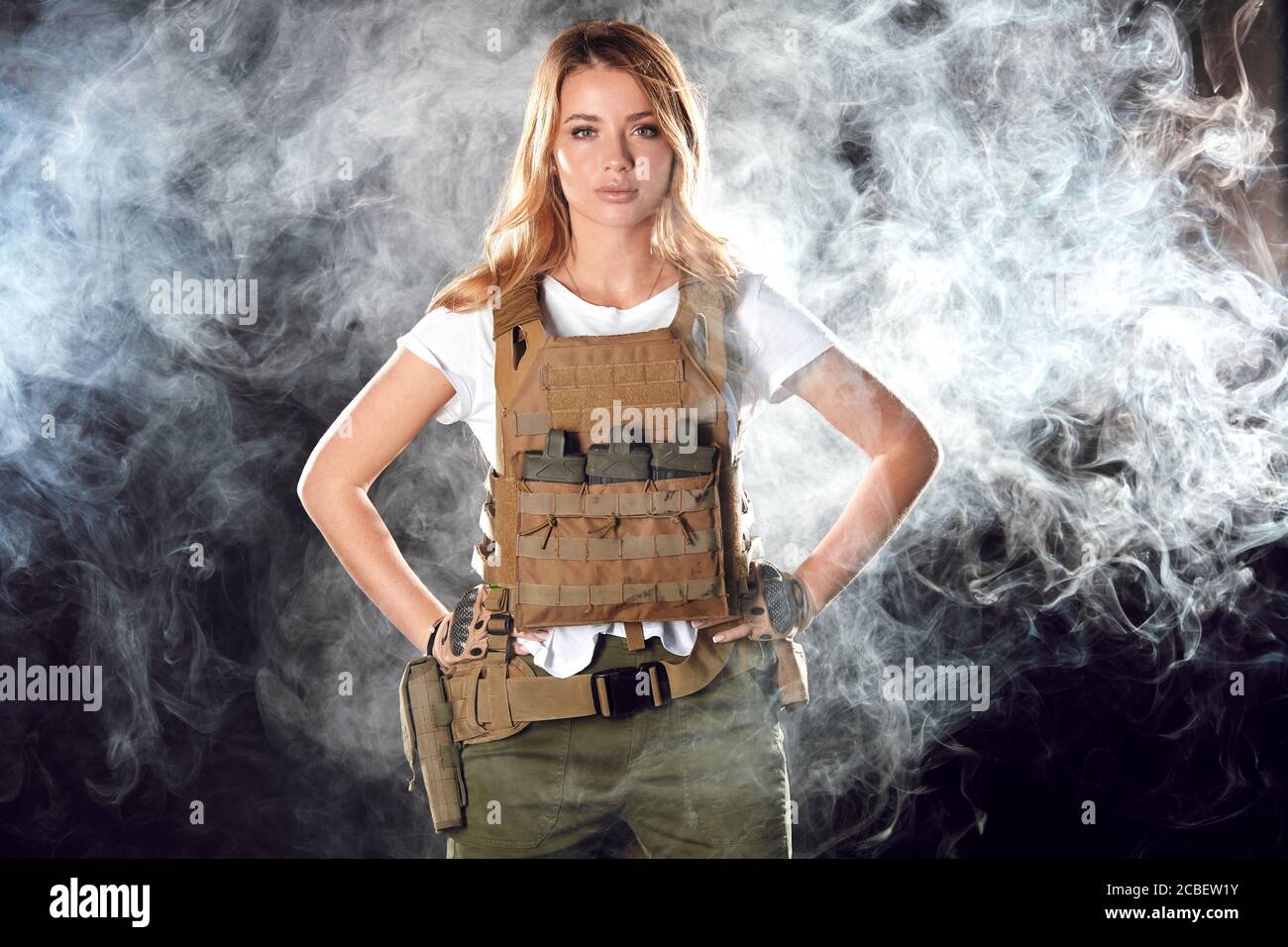 Portrait beautiful blonde female soldier dressed in plate carrier and warbelt. Women, army, weapon, technology and people concept. Black smoky backgro Stock Photo