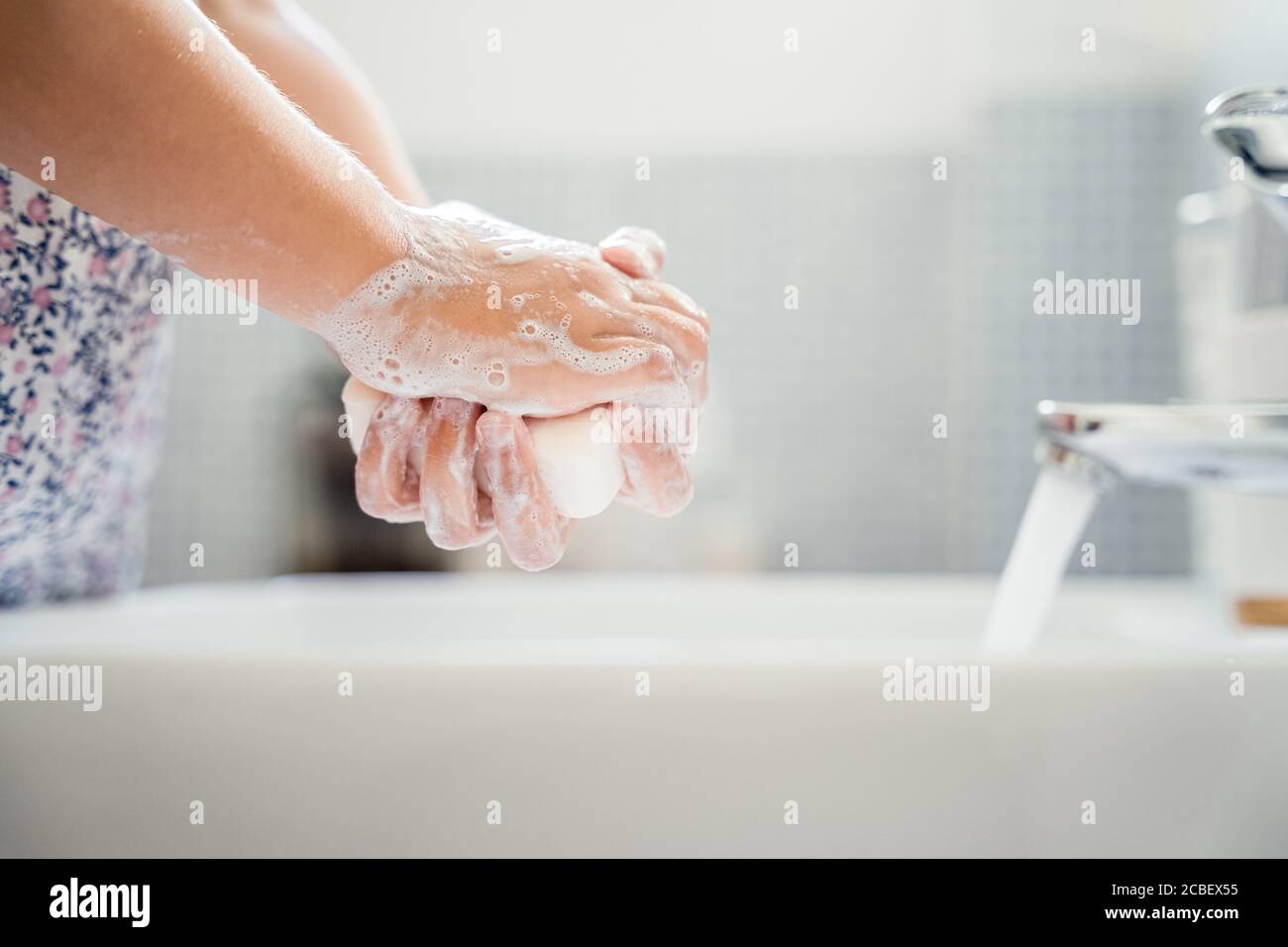 Little girl washes hands with bar of soap in washbasin under running tap water. Close up, detail Stock Photo