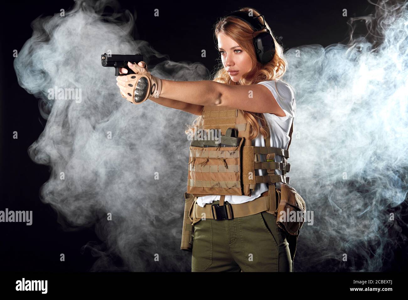 Woman in protective armour and headphones holds gun in hands, aiming
