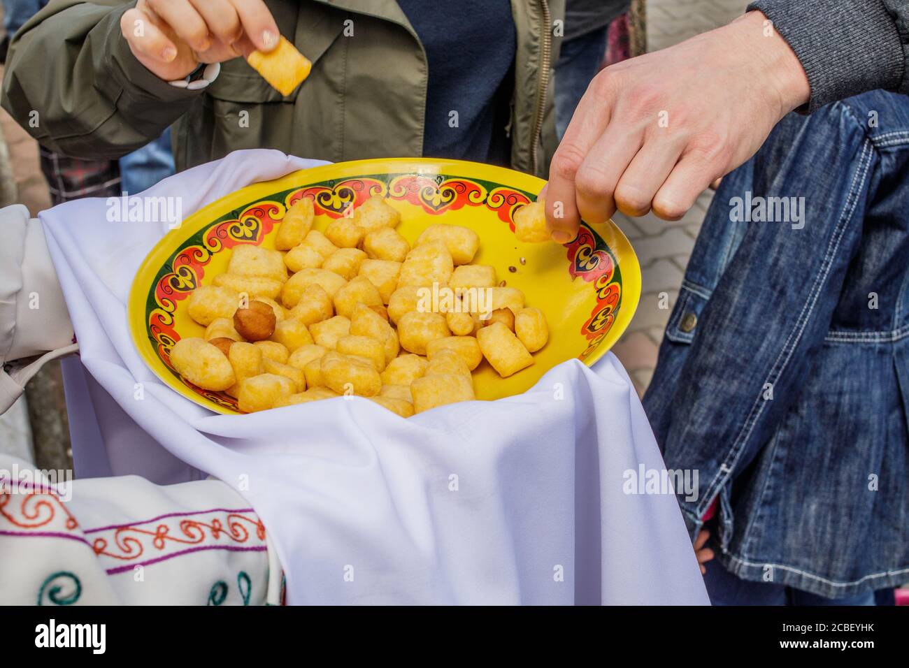 Oriental cuisine. On the hands of a person Bashkir baursak or Boortsog in a plate with an ethnic pattern. View from above. Stock Photo