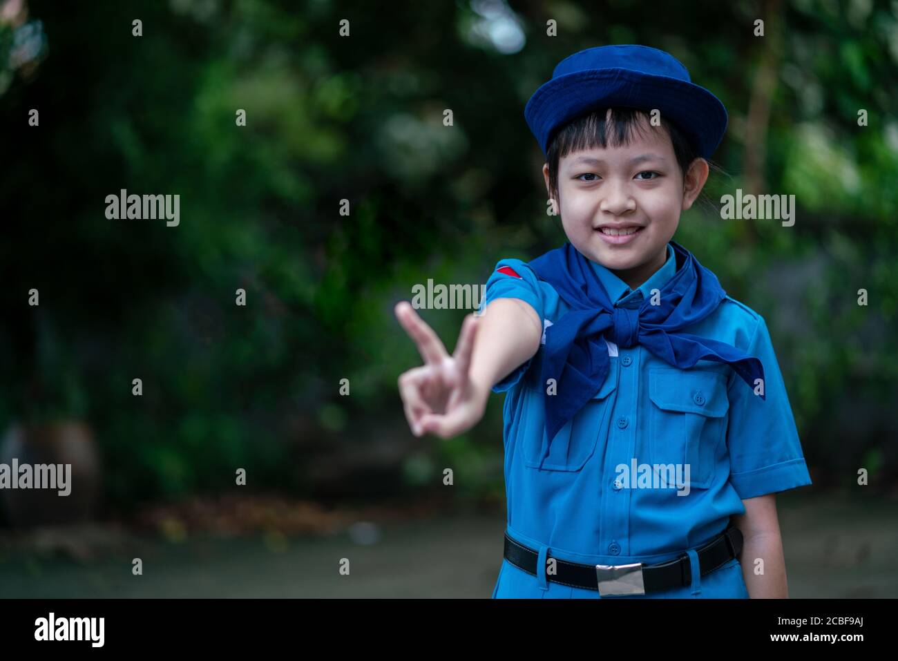 Beautiful uniform scout girl standing and showing fingers sign with happy and smile Stock Photo