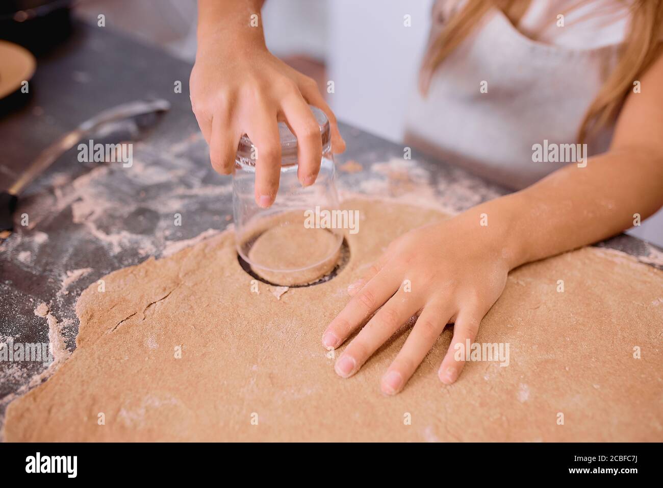 child helper forming circle forms from dough with the use of cup. Close-up hands of kid girl Stock Photo