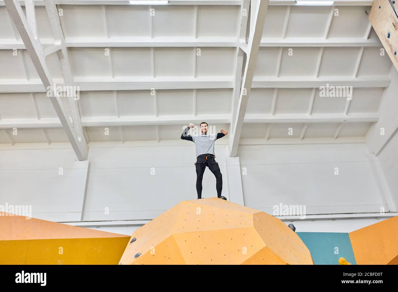 Low angle view of physically challenged young boulderer standing at the top of artificial climbing wall, extremely happy and proud of himself, well-eq Stock Photo
