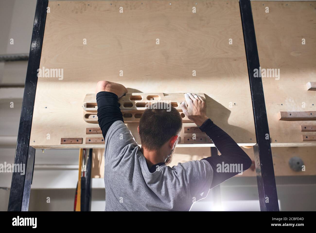 Close up view of young rock climber without forearm hanging on special wooden panel for working out firm grip, training in indoors climbing settings. Stock Photo