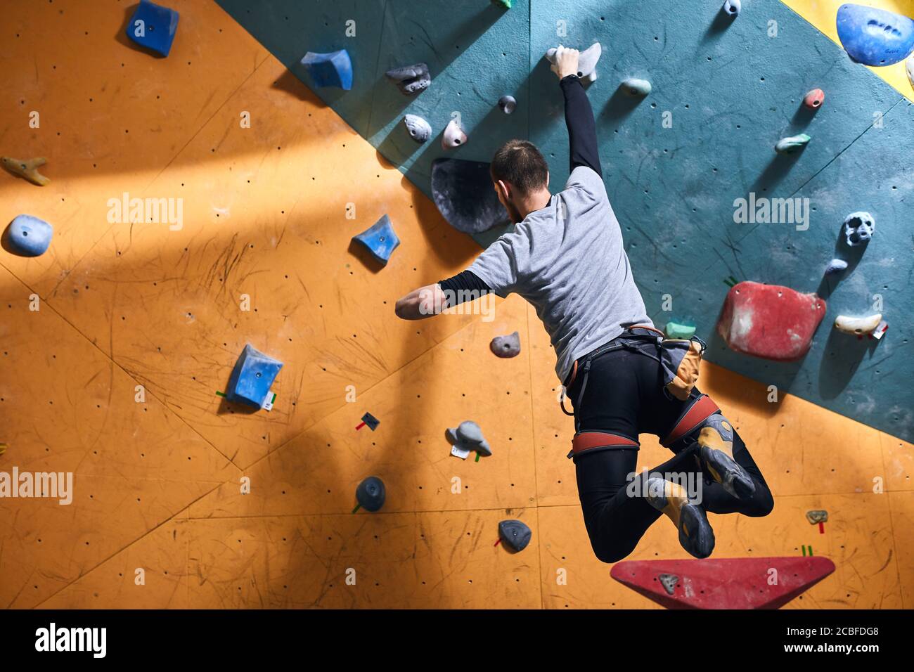 Unrecognizable powerful boulderer with physical disability hanging at climbing wall, balancing on one hand, has sporty muscled body, strong-willed, lo Stock Photo