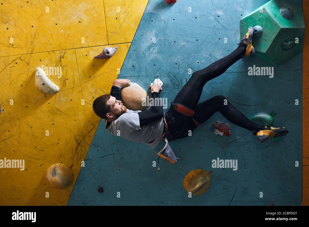 Side view of motivated active physically challenged boulderer with beard hanging at colourful climbing wall, holding large artificial rock, trying to Stock Photo