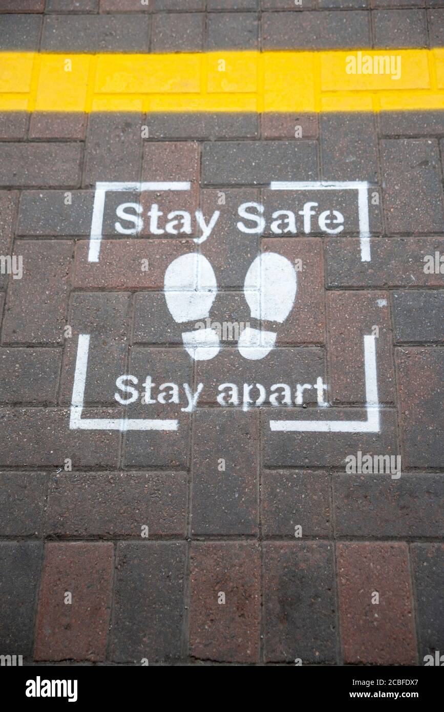 Stay safe stay apart, stencilled paint warning sign, including footprints, on Wigan northwestern train station platform during COVID-19 local lockdown. Stock Photo