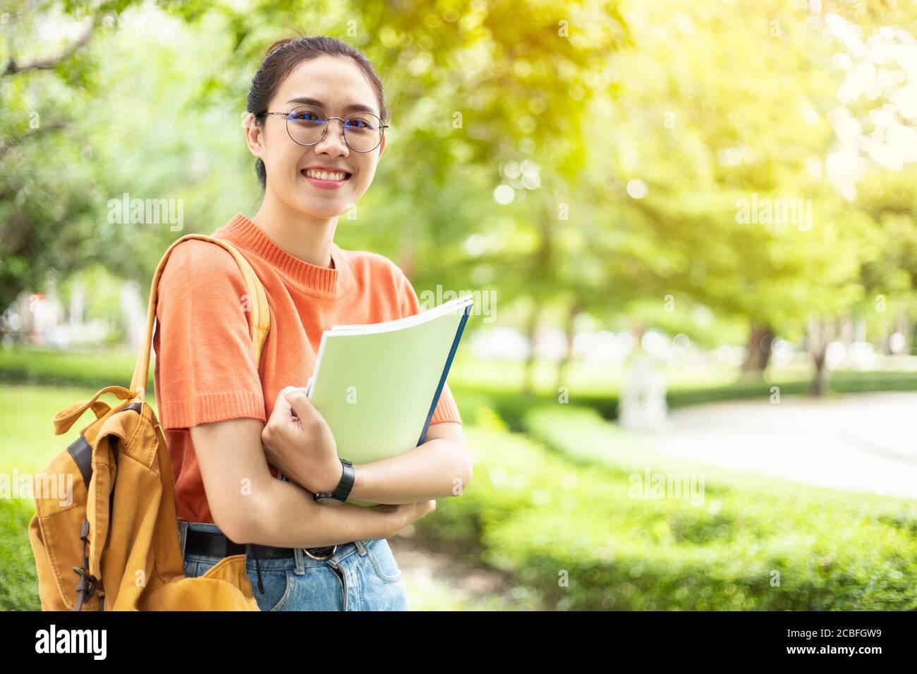 Portrait of nerd Asian woman girl smart teen happy smiling with glasses at green park outdoor in university campus with copyspace Stock Photo