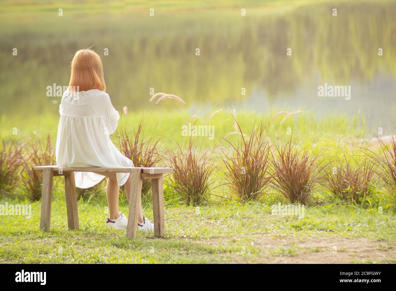 lonely child girl blonde hair sitting at quiet peace lake alone at the morning back view Stock Photo
