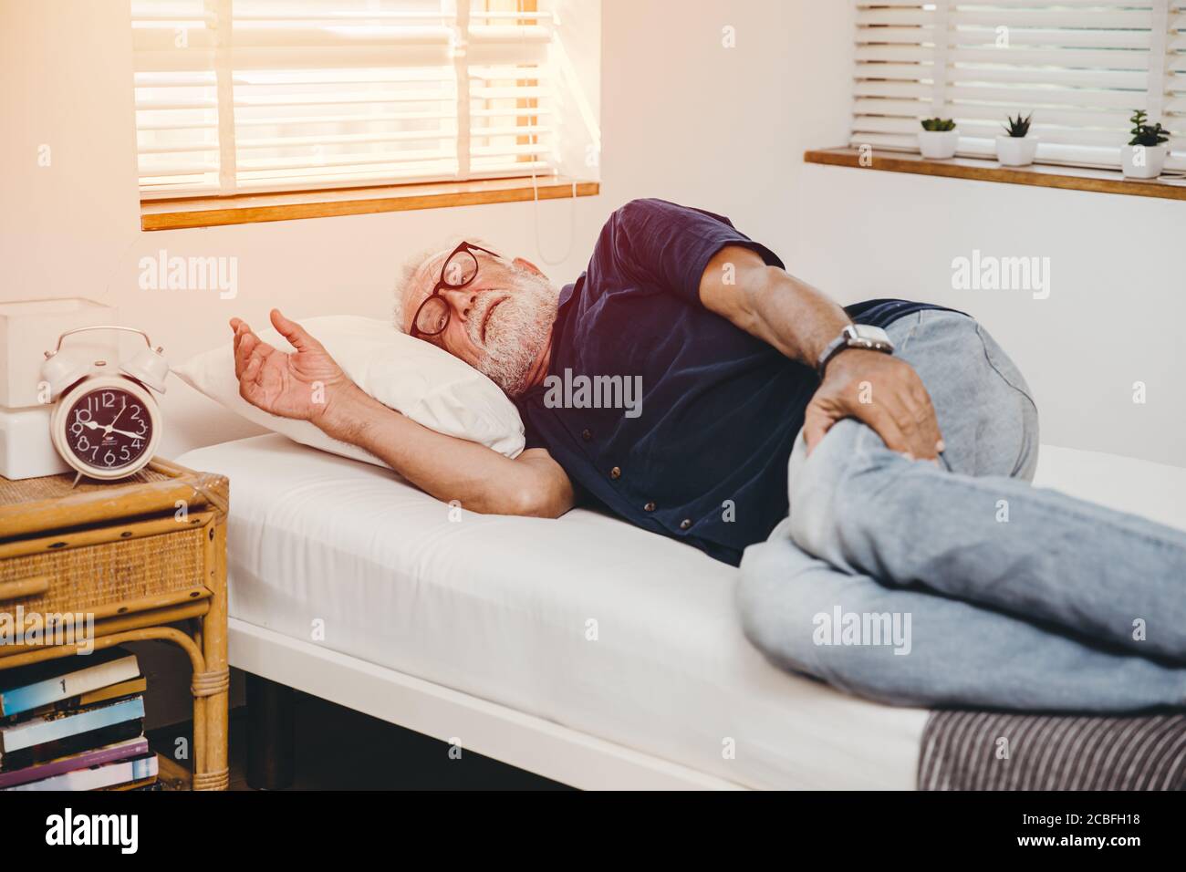 Old man lay in bed with hand holding pain in his legs alone at home