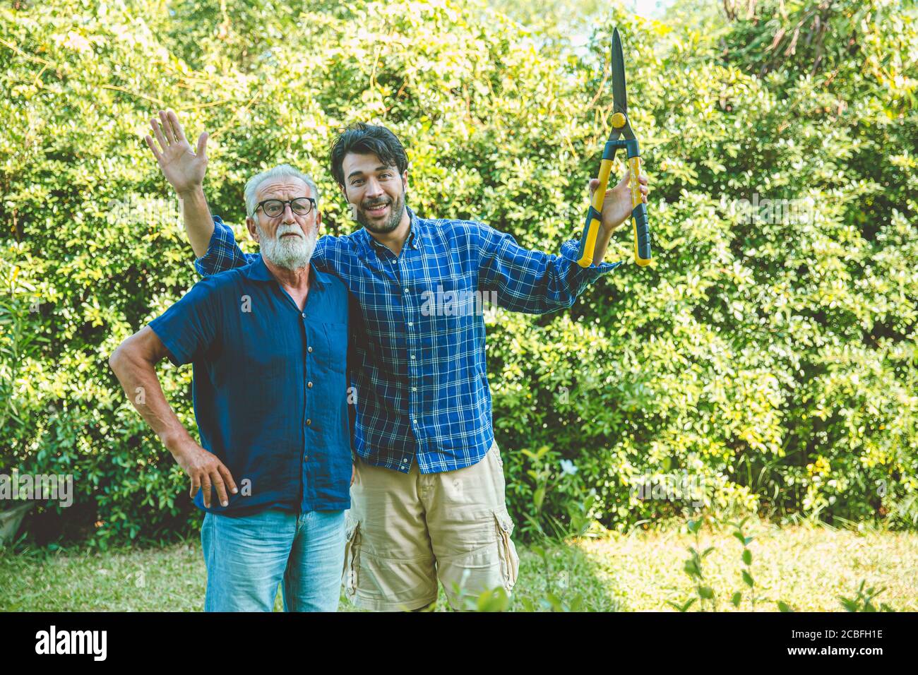 Happy gardener, elder with man enjoy pruning bushes at backyard for stay home activity in holiday looking camera Stock Photo