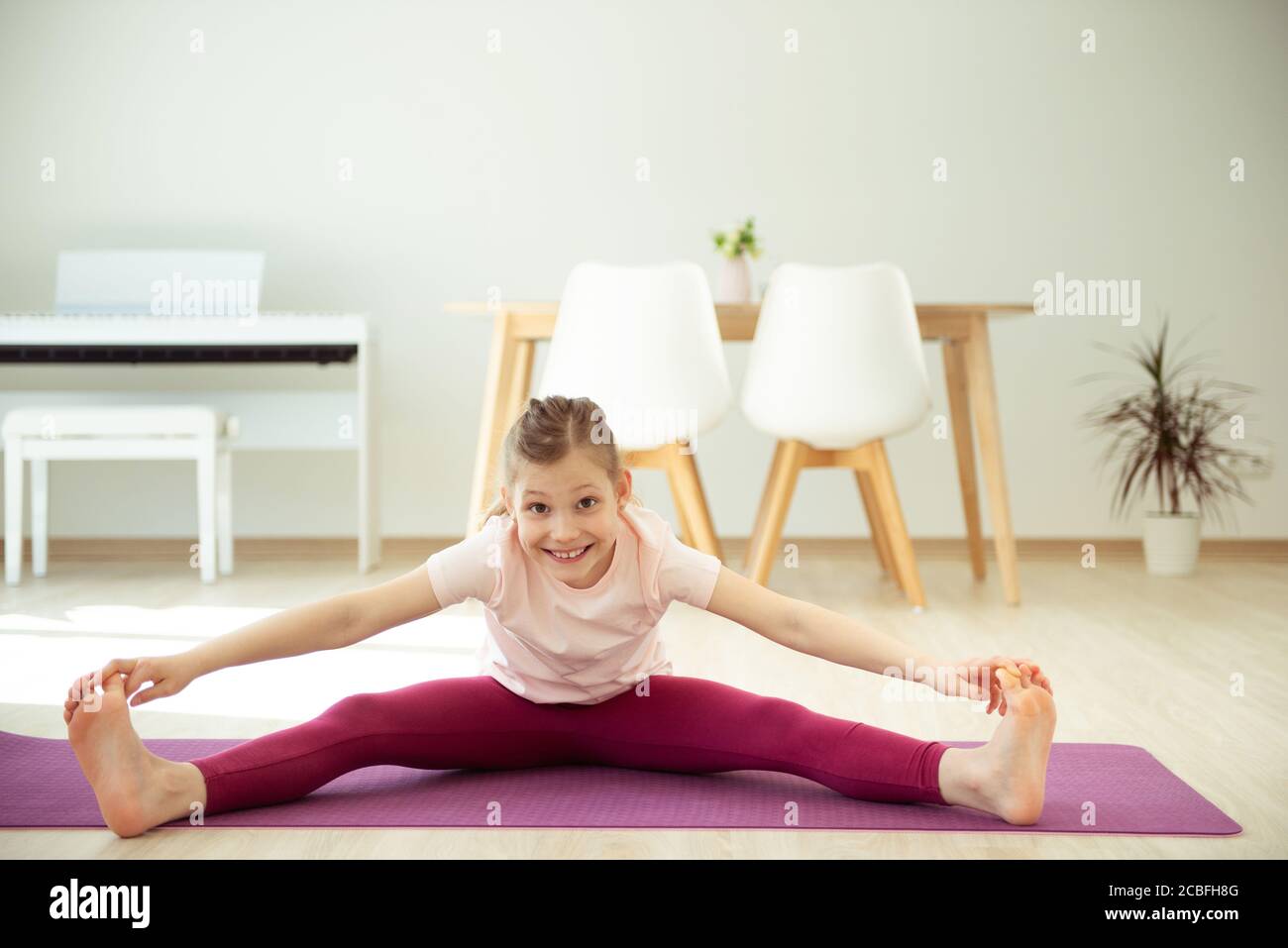 Pretty happy teen child girl having fun making yoga stretch exercises ...